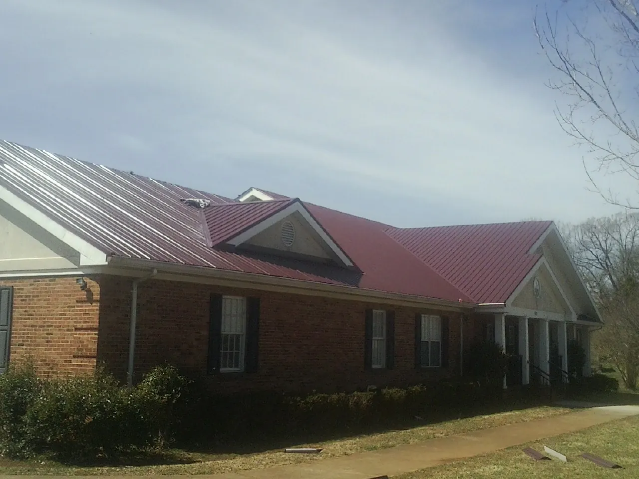 Red metal roof with gabled entries on a long brick building, from a Hail Damage Roof Repair job in Ambler