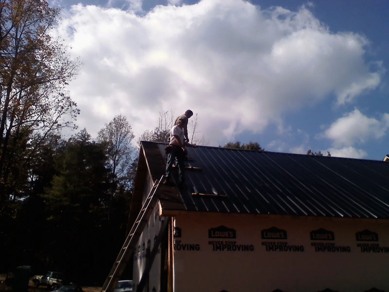 Roofer fastening dark metal panels high against a cloudy sky, from a Roof Inspection job in Ambler