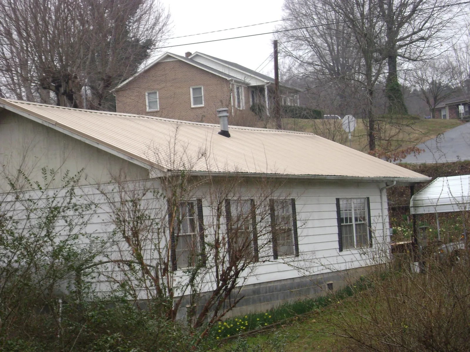 Tan metal roof on a white sided house set into a hillside — Commercial Roofing by Roofing Brothers in Ambler